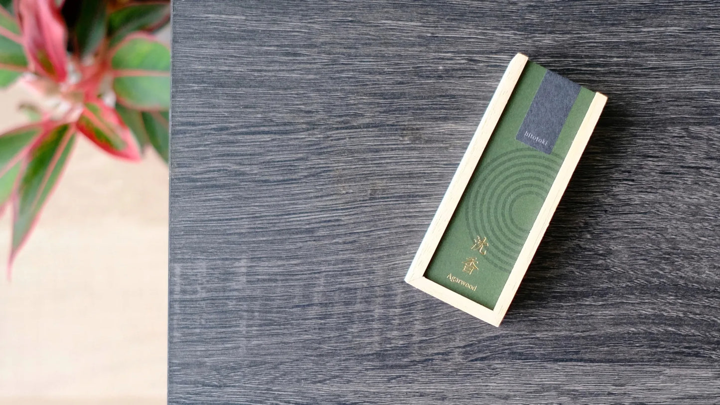 Green cover incense product packaging on a wooden surface with a plant in the corner