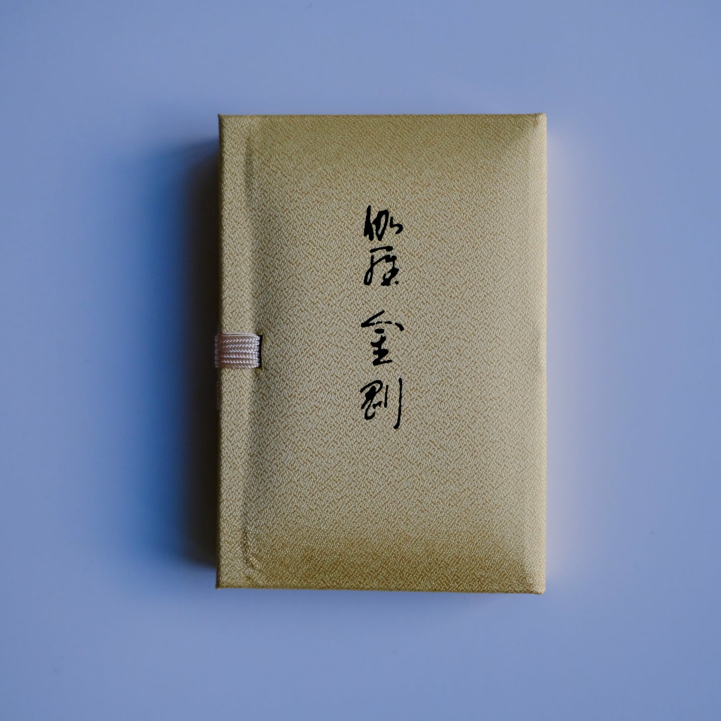 Nippon Kodo Kyara Kongo incense in its elegant, fabric-covered Paulownia wood box. The box is cream-colored with Japanese calligraphy, and a small purple ribbon is visible on the side. This premium Japanese incense is made from selected aloeswood and includes 60 sticks with a ceramic holder.