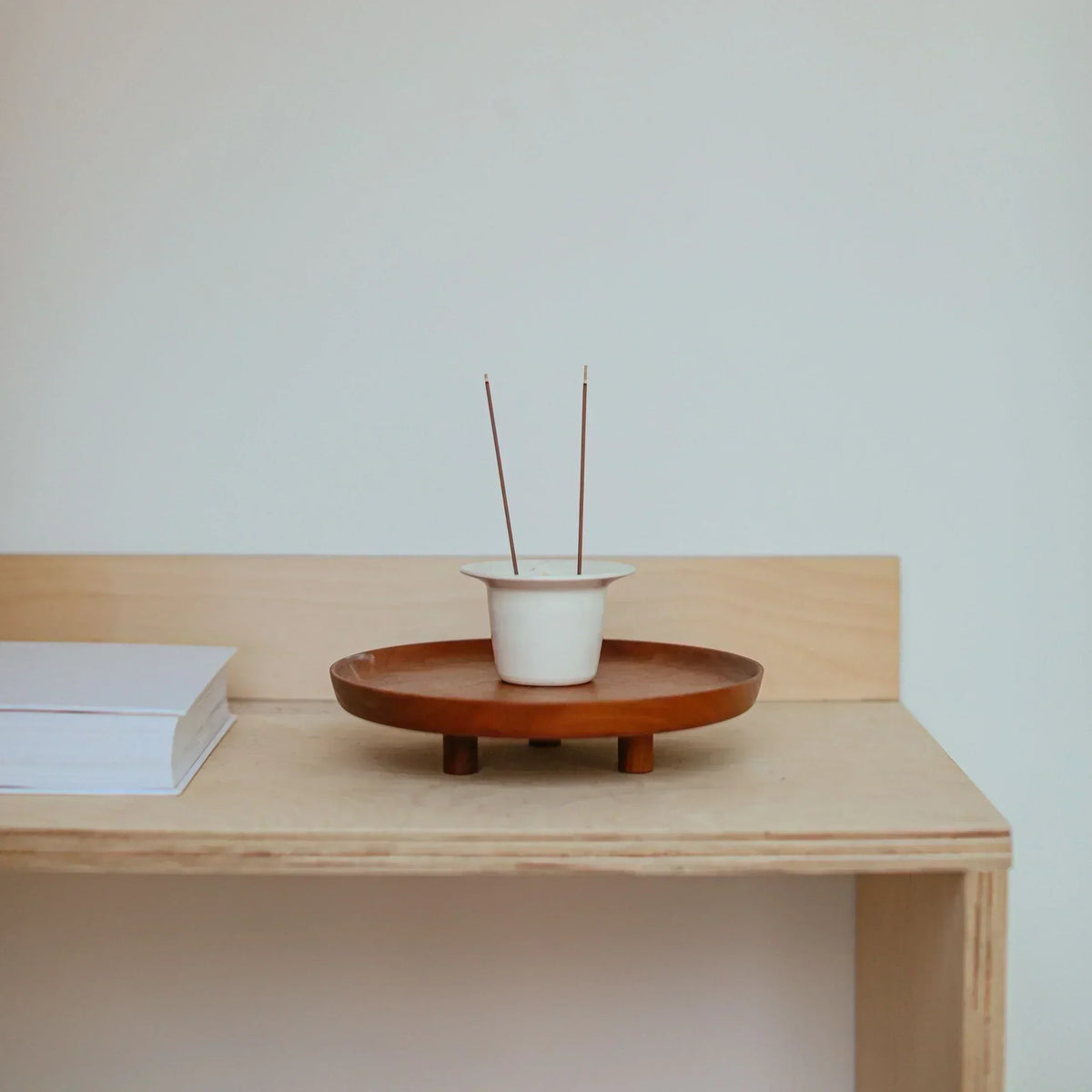 Two incense sticks standing in a white holder on a wooden tray.