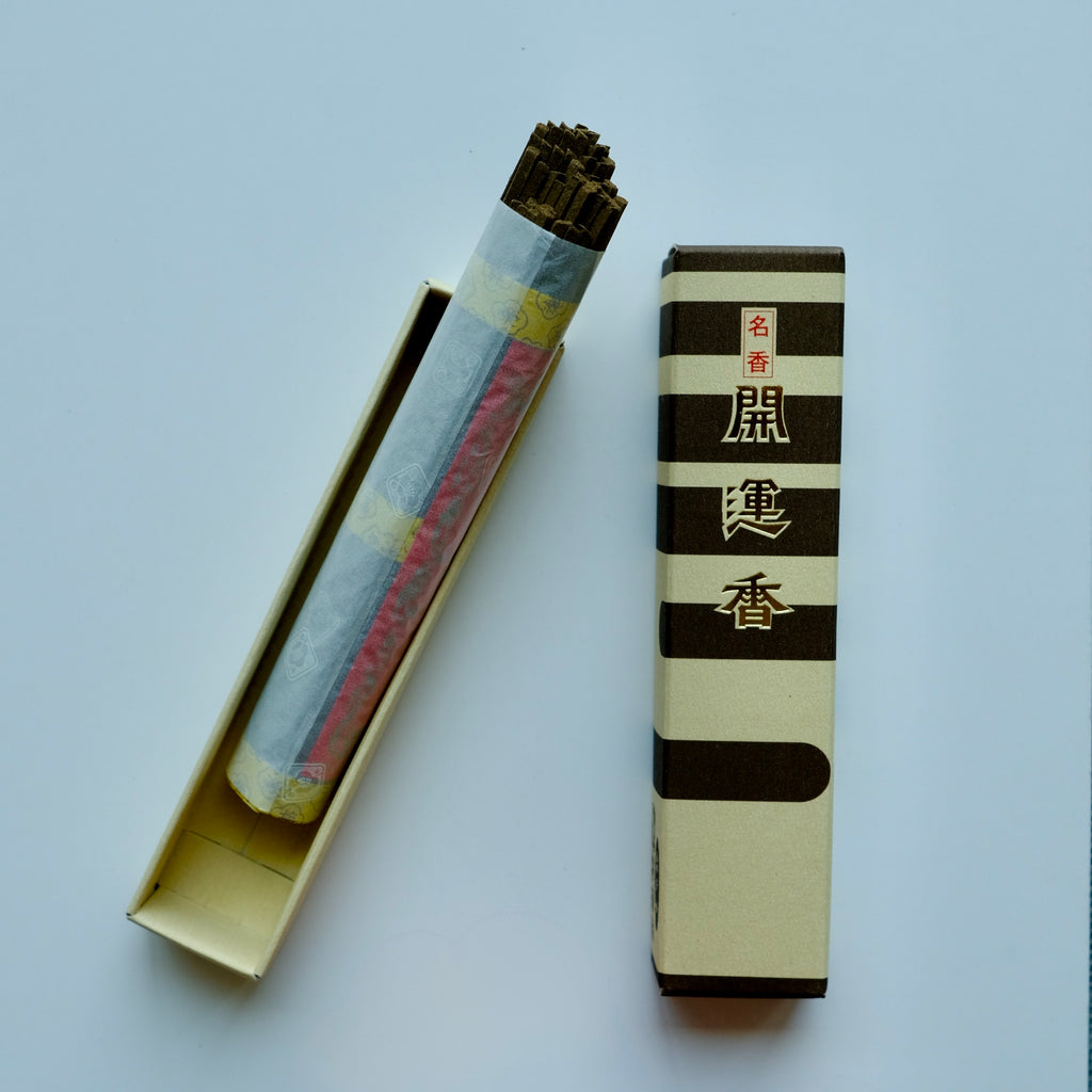 Baieido Kai Un Koh incense with the box opened to show the bundle of sticks in the inner tray, placed next to the striped outer sleeve."