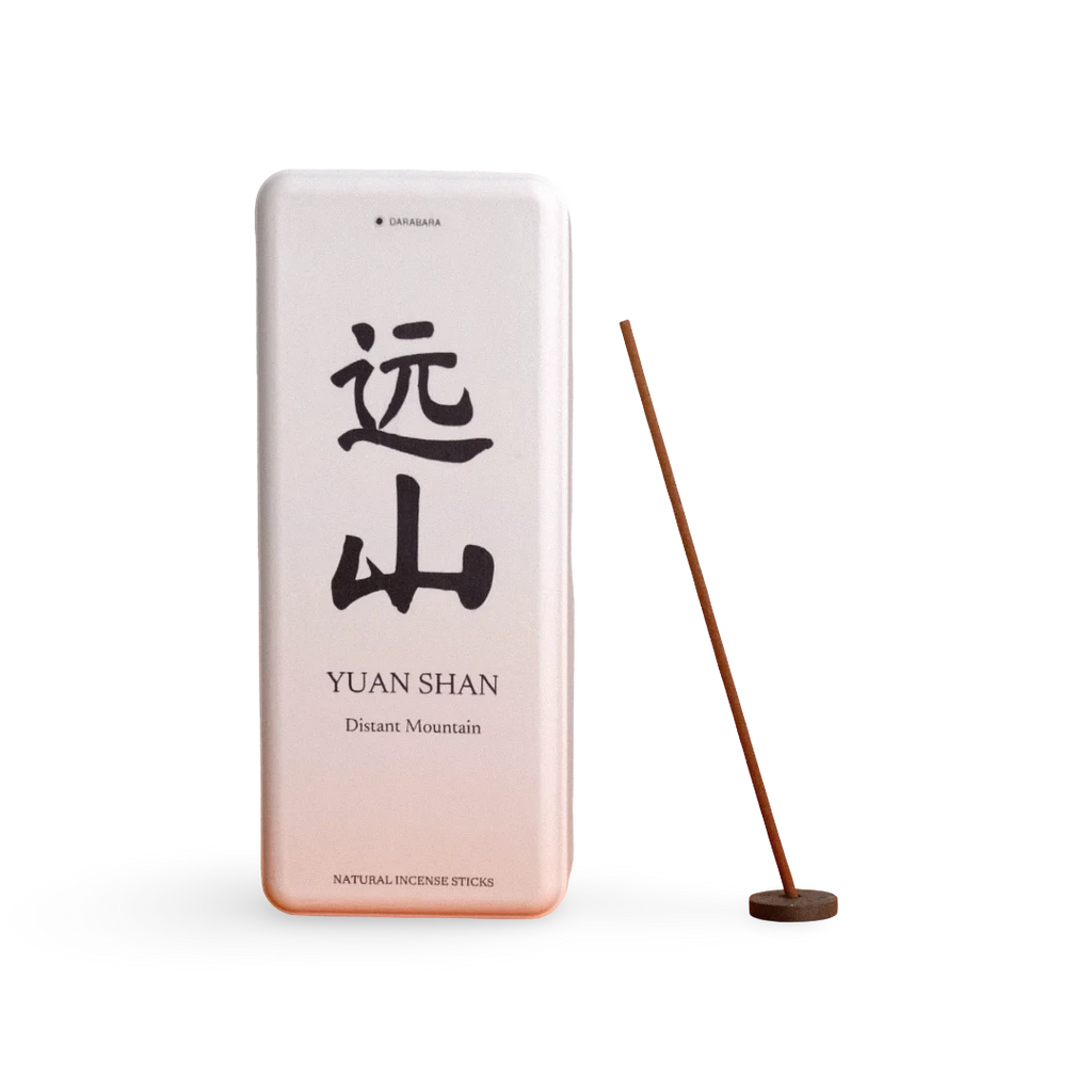 A rectangular metal incense tin labeled 'YUAN SHAN' with large black Chinese characters and smaller English text, shown next to a single incense stick on a round wooden holder against a clean white background.