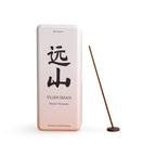 A rectangular metal incense tin labeled 'YUAN SHAN' with large black Chinese characters and smaller English text, shown next to a single incense stick on a round wooden holder against a clean white background.