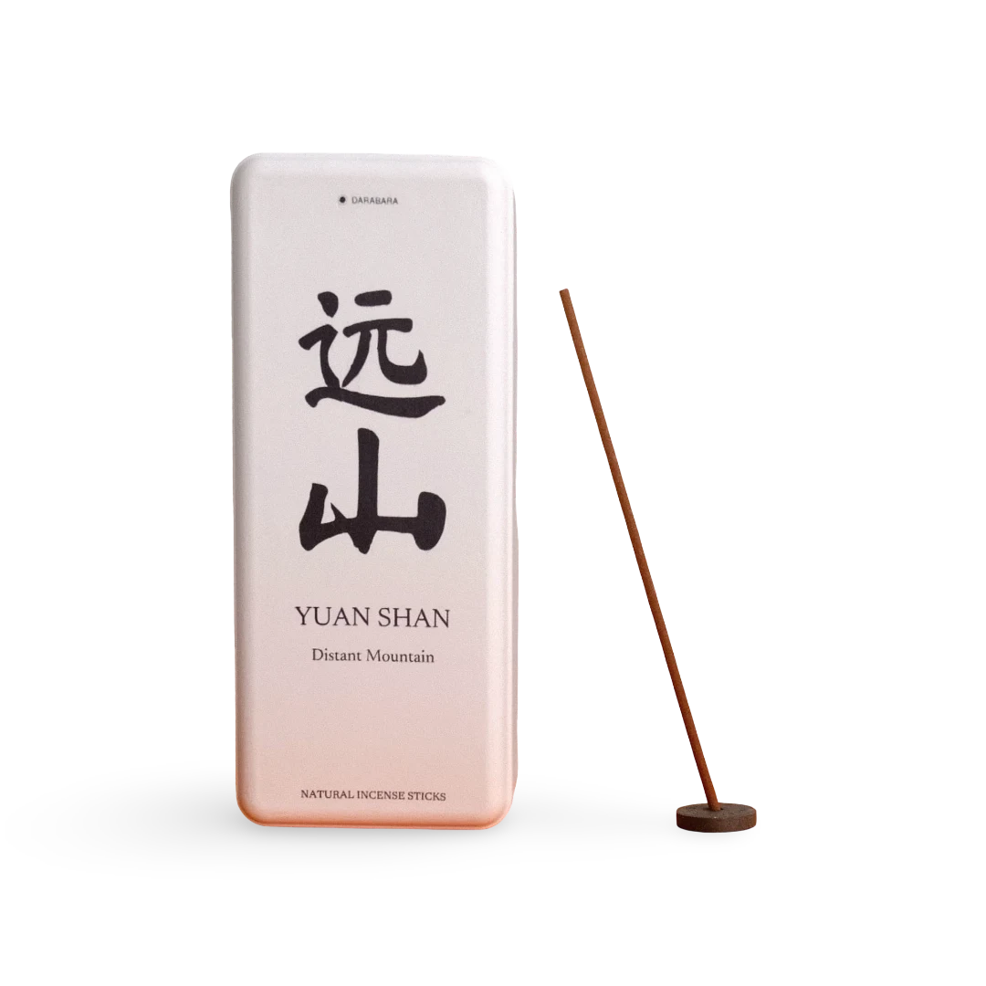 A rectangular metal incense tin labeled 'YUAN SHAN' with large black Chinese characters and smaller English text, shown next to a single incense stick on a round wooden holder against a clean white background.
