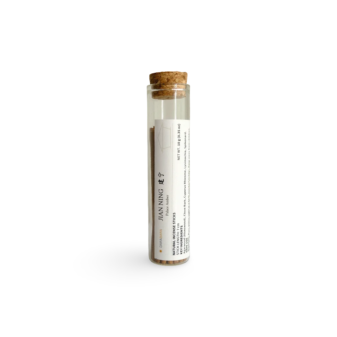 A clear glass tube with a cork stopper and a white label reading JIAN NING Incense, containing brown herbal powder, photographed on a clean white background.