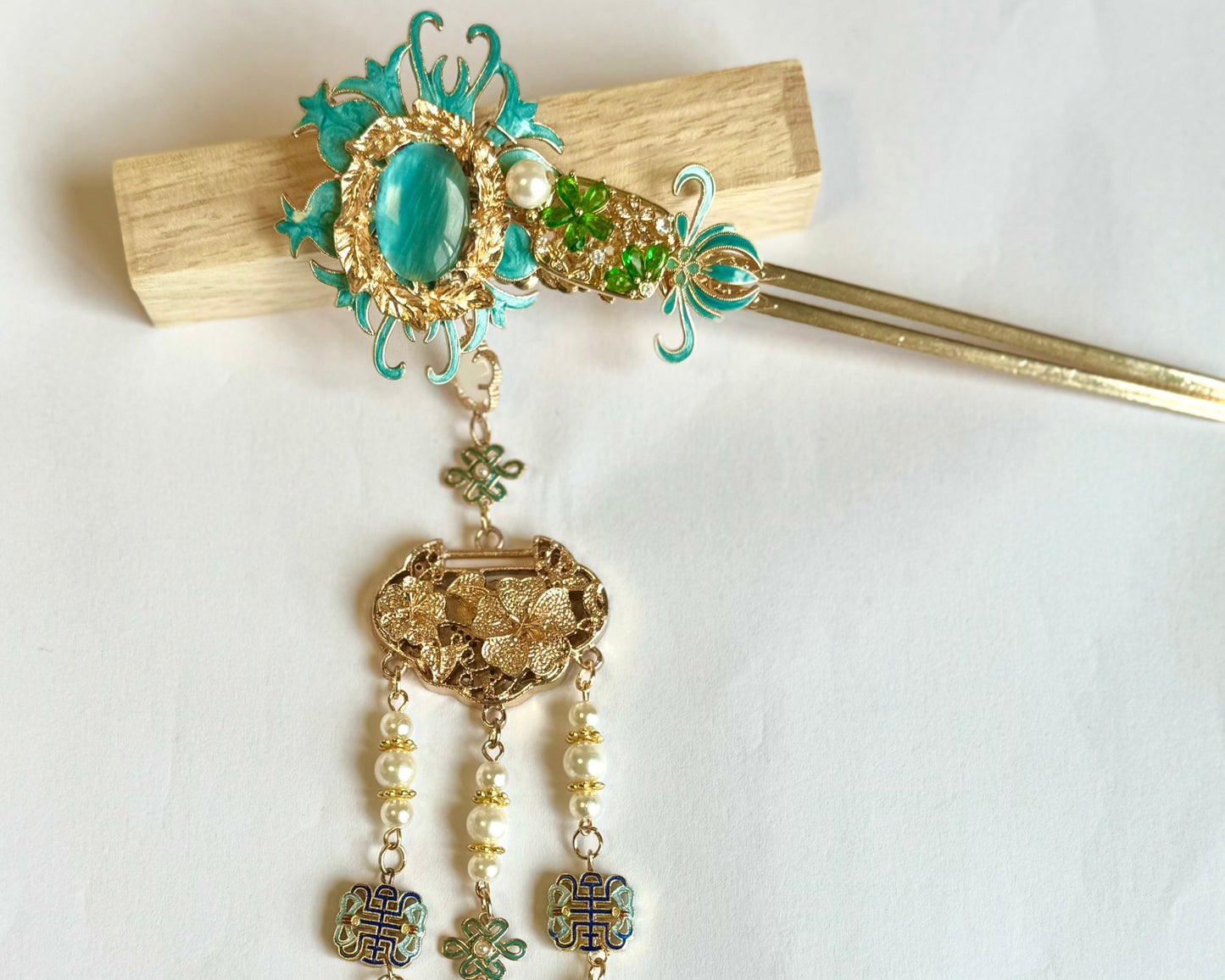 Jade Garden traditional Chinese hair pin featuring ornate turquoise enamel and gold-tone detailing. This elegant hair pin showcases a vintage-inspired design with a central jade-colored cabochon surrounded by filigree work, cascading into three strands of delicate pearl beads and verdigris leaf charms. The decorative hair ornament combines classical Asian aesthetics with antique brass finish, ornamental Celtic knots, and dangling elements that create gentle movement. Perfect for traditional cere