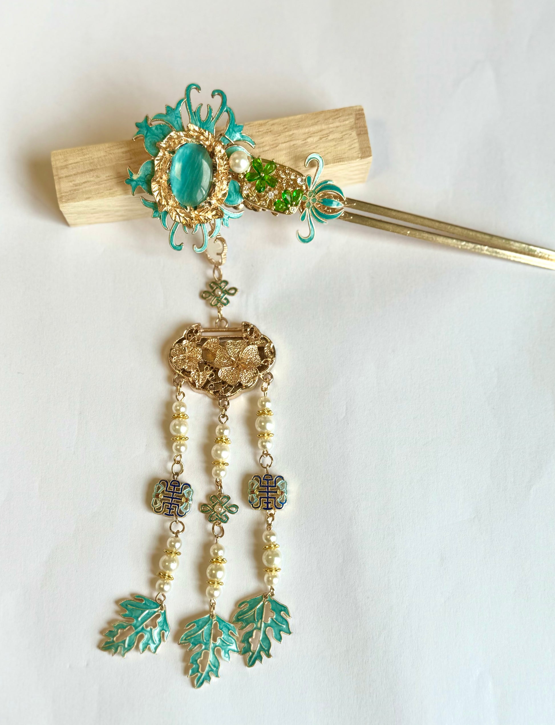 Jade Garden traditional Chinese hair pin featuring ornate turquoise enamel and gold-tone detailing. This elegant hair pin showcases a vintage-inspired design with a central jade-colored cabochon surrounded by filigree work, cascading into three strands of delicate pearl beads and verdigris leaf charms. The decorative hair ornament combines classical Asian aesthetics with antique brass finish, ornamental Celtic knots, and dangling elements that create gentle movement. Perfect for traditional cere