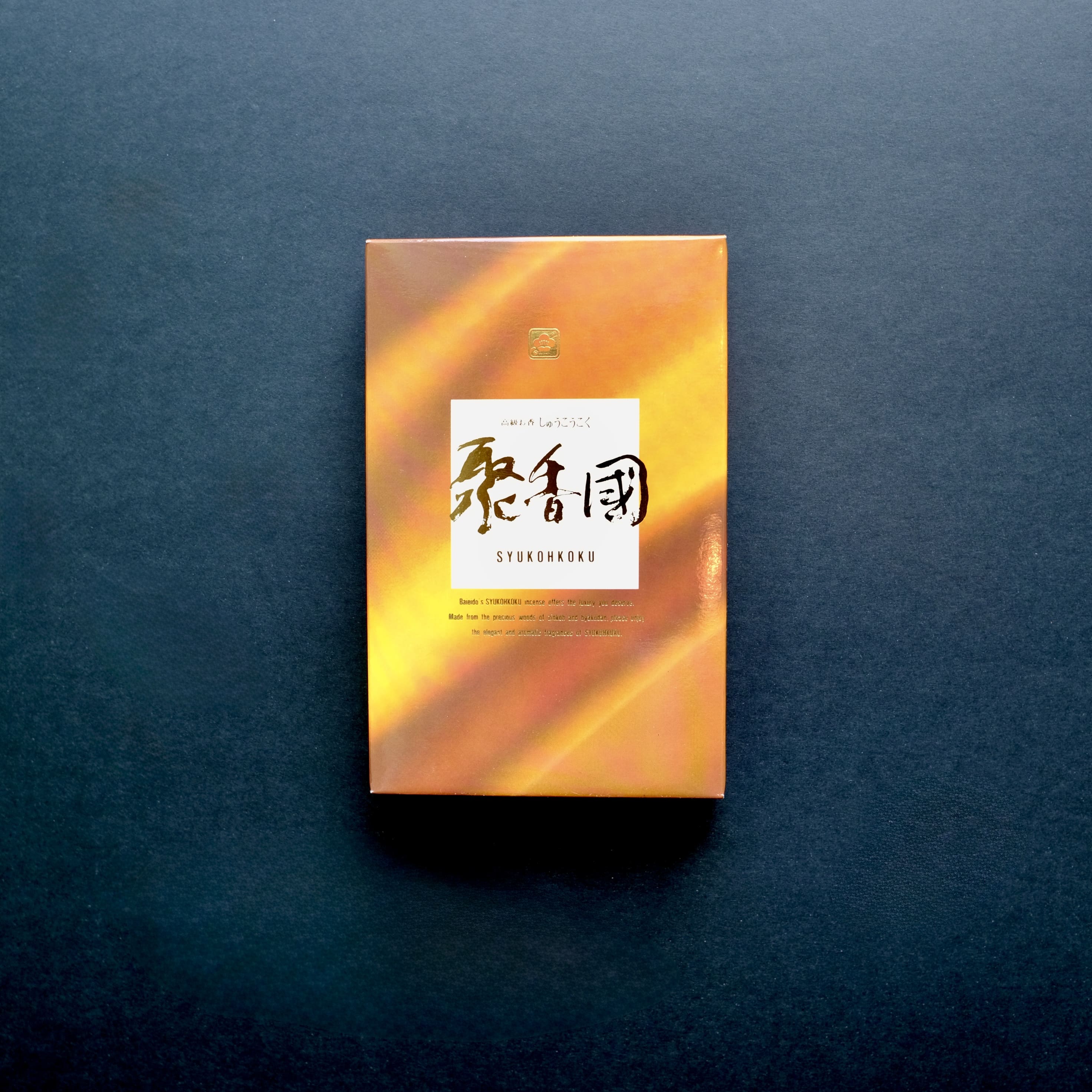The front of the premium Baieido Shukohkoku incense box, featuring a golden-orange design and a central white label with Japanese calligraphy.