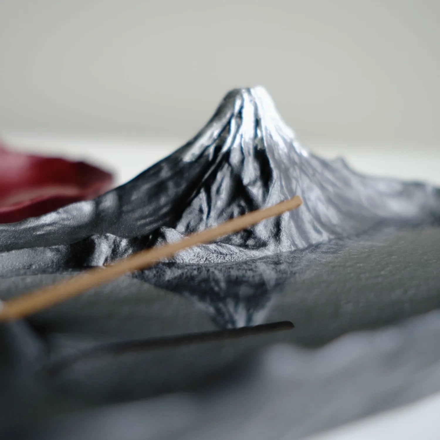 Close-up of black Sakasa Mt. Fuji incense holder with incense stick and mountain reflection
