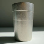Textured tin tumbler cup on a gray surface with a neutral background