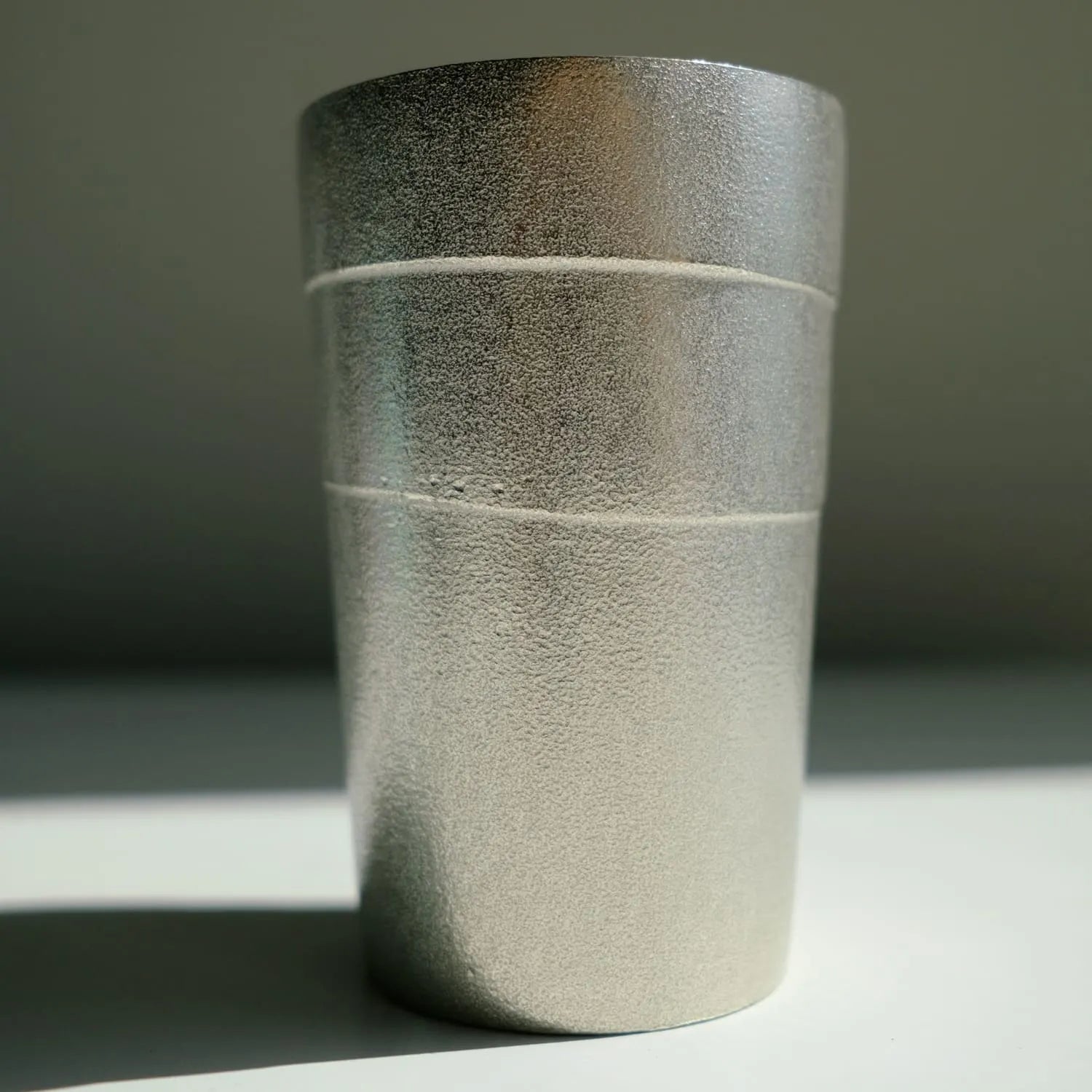 Textured tin tumbler cup on a gray surface with a neutral background