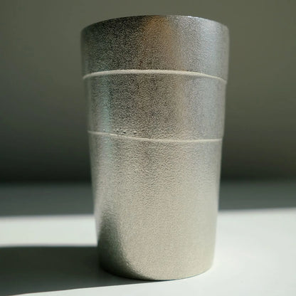 Textured tin tumbler cup on a gray surface with a neutral background