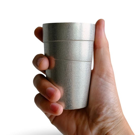 Hand holding a silver tin cylindrical beer tumbler with circular lines against a transparent background