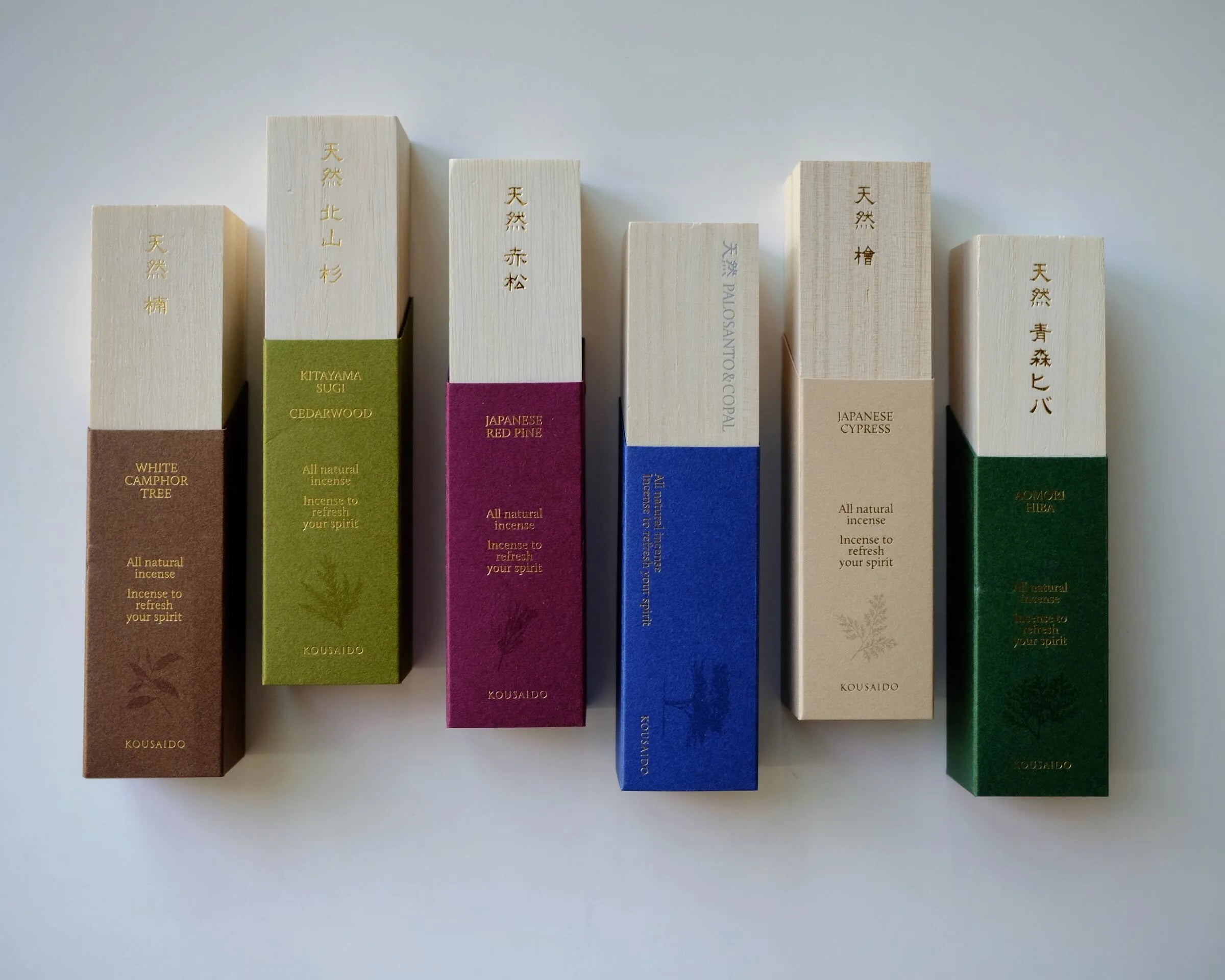 Set of wooden boxes of Kousaido Tennen Natural incenses with different colored bands on a white background