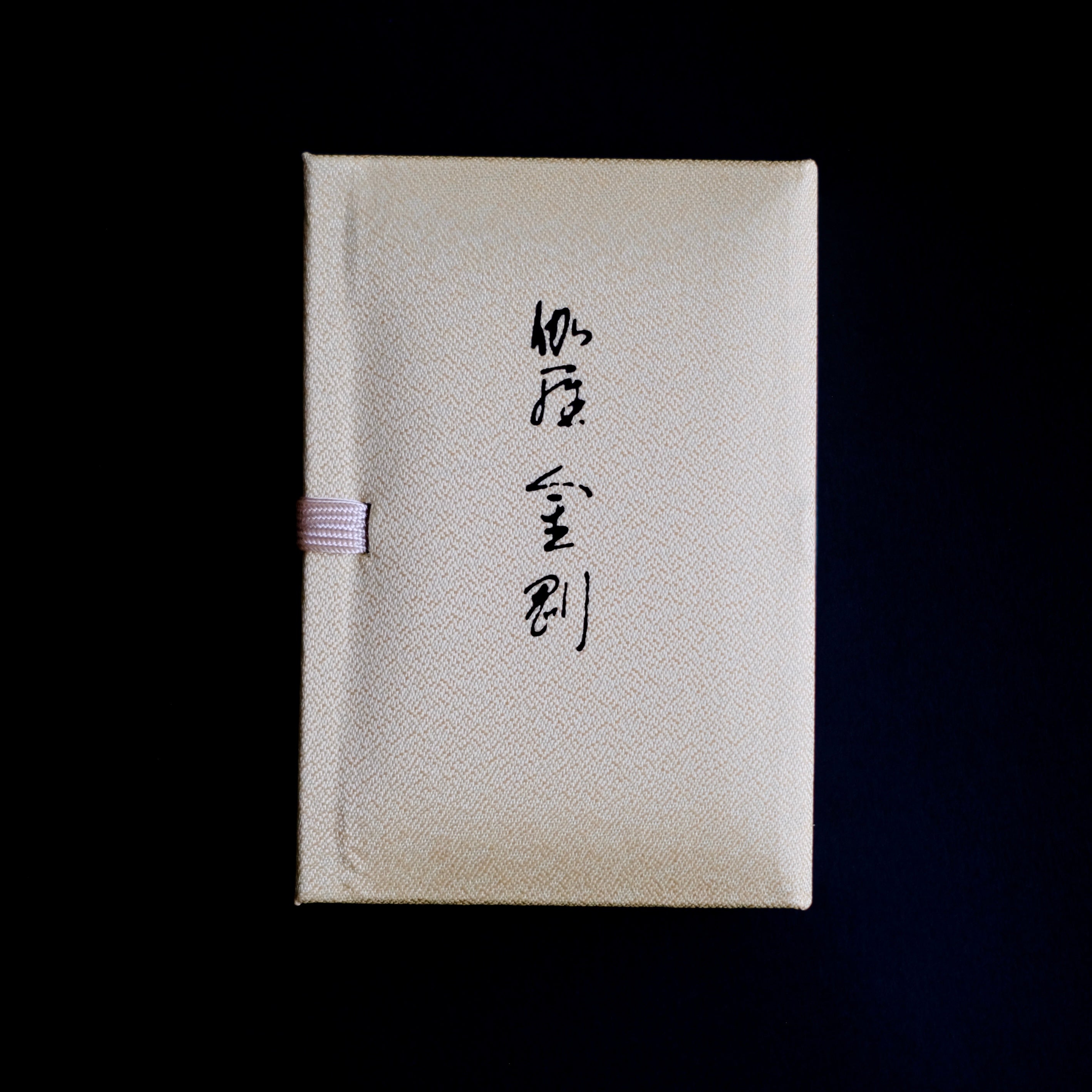 Nippon Kodo Kyara Kongo incense in its elegant, fabric-covered Paulownia wood box. The box is cream-colored with Japanese calligraphy, and a small purple ribbon is visible on the side. This premium Japanese incense is made from selected aloeswood and includes 60 sticks with a ceramic holder.