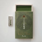 Green matchbox with intricate design and matches on a light gray background