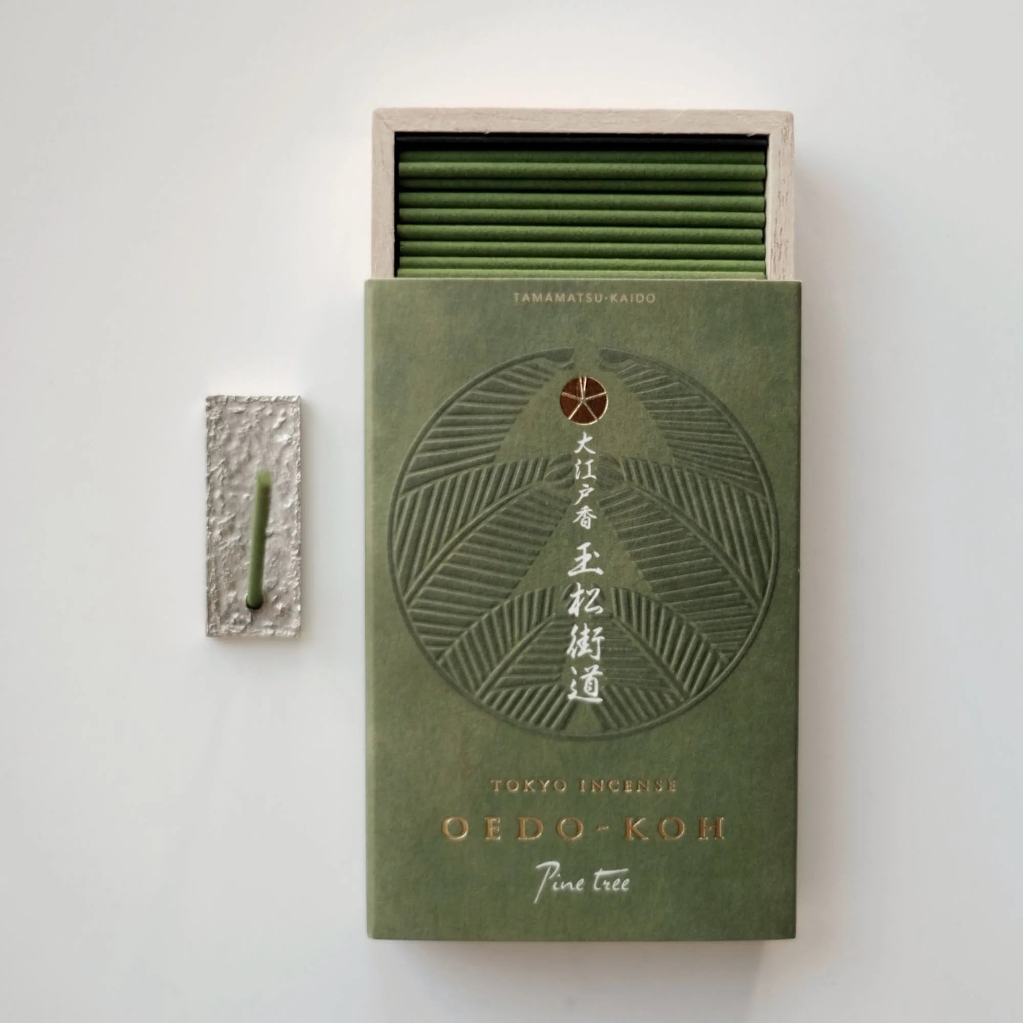 Green matchbox with intricate design and matches on a light gray background