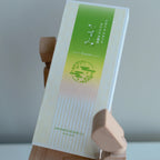 Box of Incense with green design on a wooden hand-shape stand against a gray background