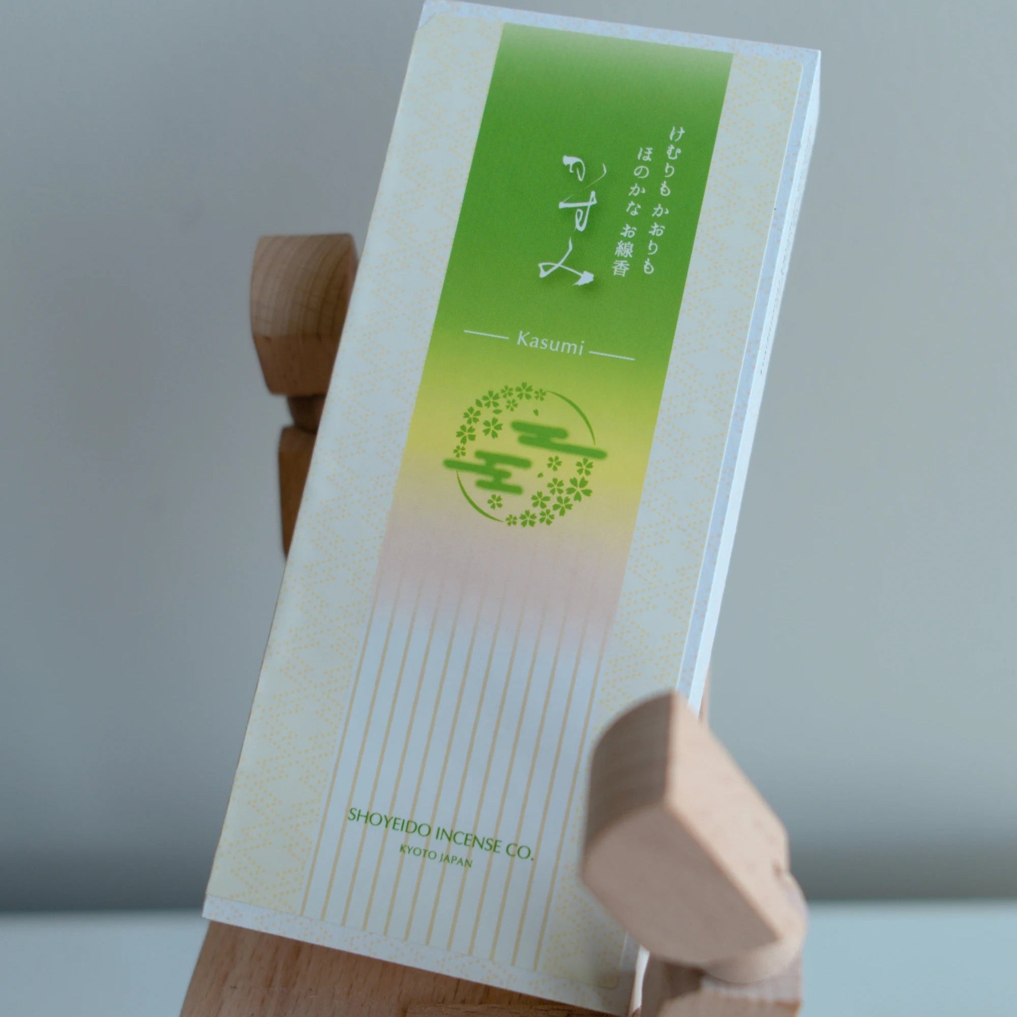 Box of Incense with green design on a wooden hand-shape stand against a gray background