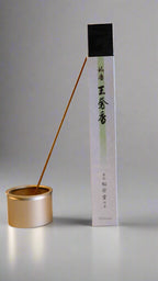 A package of Shoyeido Premium Series incense with a single incense stick burning, alongside a gold-colored burner.