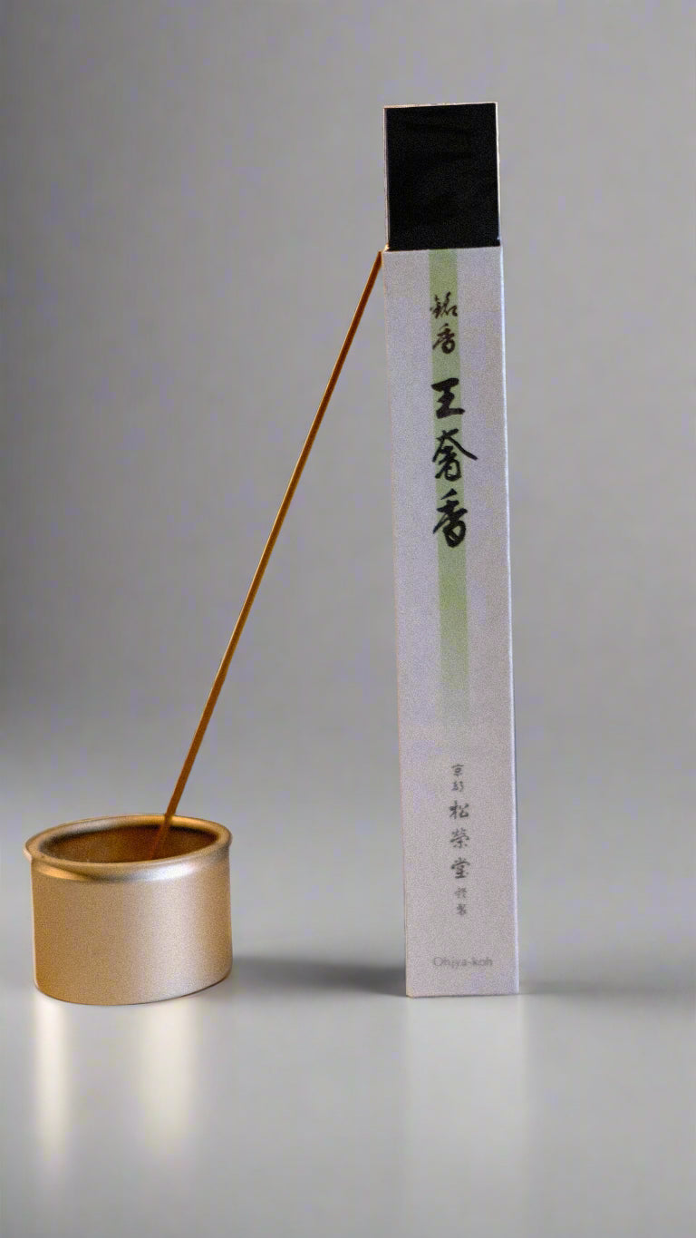 A package of Shoyeido Premium Series incense with a single incense stick burning, alongside a gold-colored burner.
