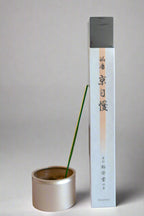 A package of Shoyeido Kyojiman incense with a single incense stick burning in a metal holder, against a white background with a floral pattern.