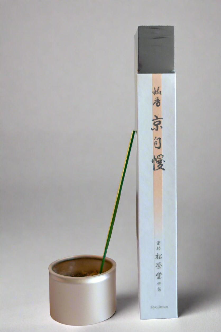 A package of Shoyeido Kyojiman incense with a single incense stick burning in a metal holder, against a white background with a floral pattern.