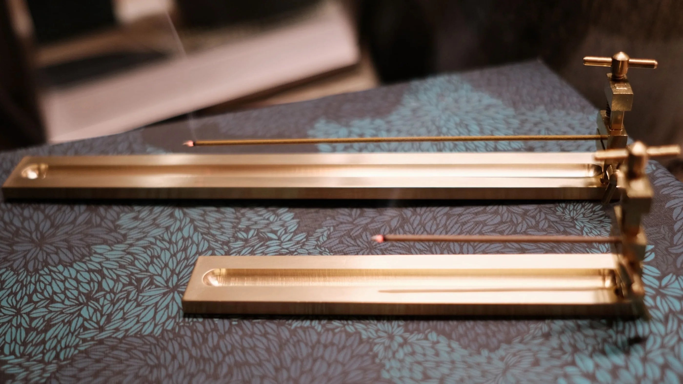 Brass metal incense holders on a textured surface, with burning incense sticks
