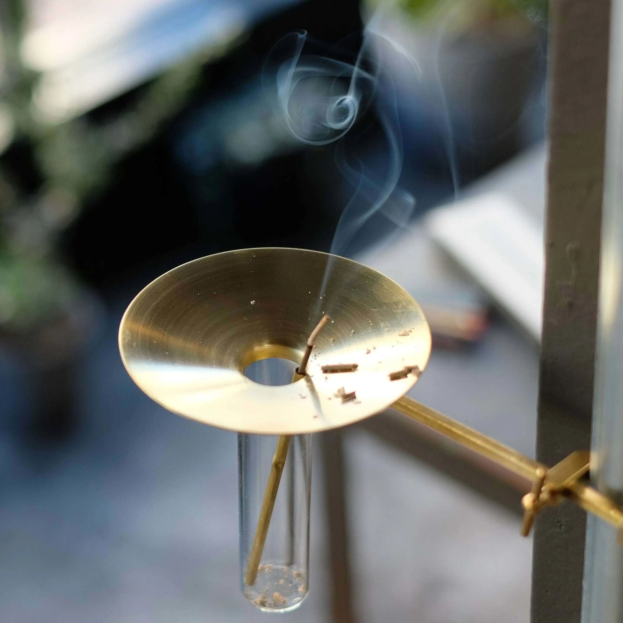 Gold incense burner tray with incense smoke rising against a blurred background
