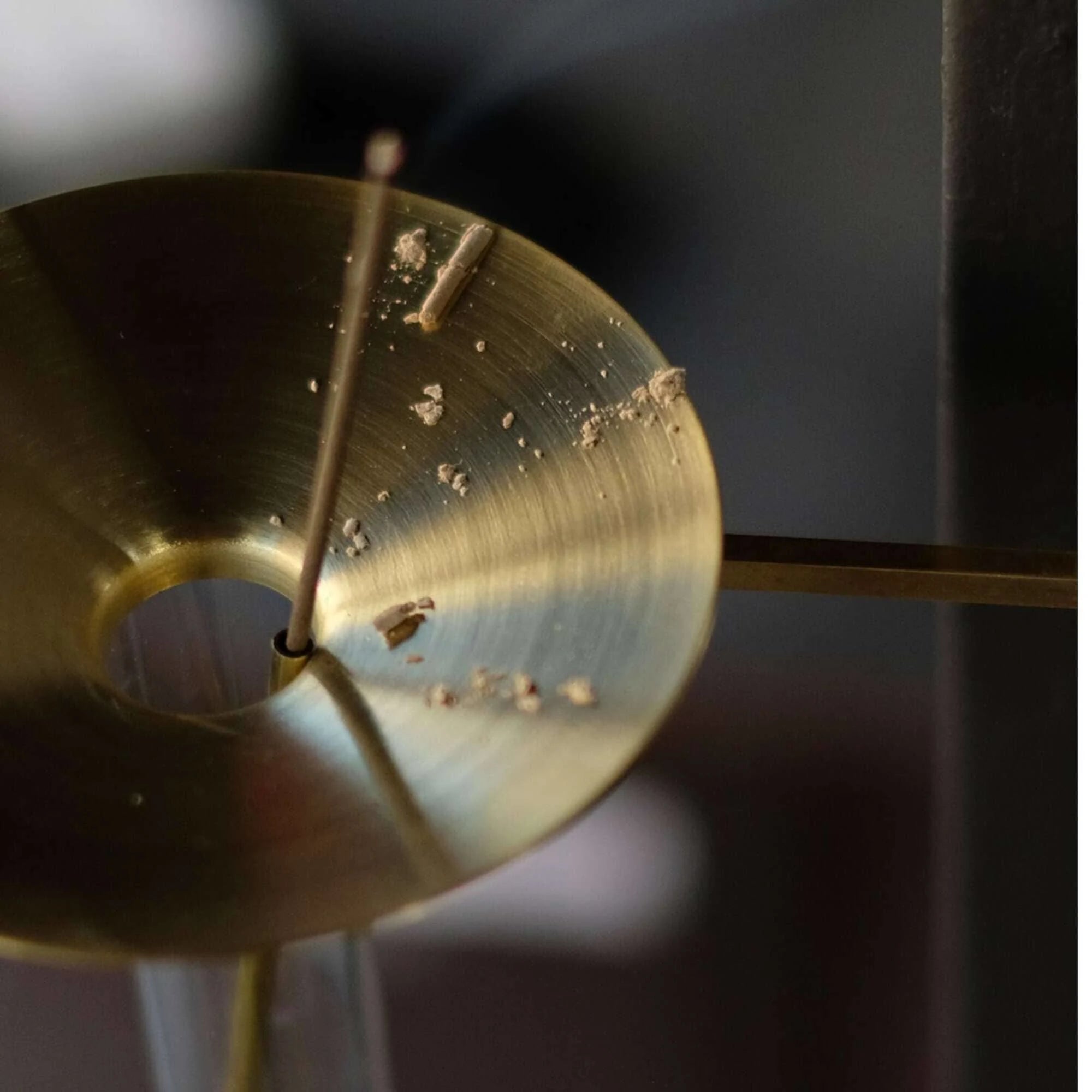 Close-up of a brass anvil incense tray with a burning incense stick blurred out of focus